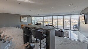 A modern interior with a high ceiling, a central table with chairs, and large windows offering a city view. - Luxury Living | Skyline Views | Grandview Retreat (Pittsburgh)