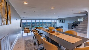 A modern dining area with a long table, chairs, and a view of a cityscape. - Luxury Living | Skyline Views | Grandview Retreat (Pittsburgh)