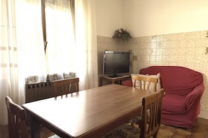 Zona de menjador amb taula i cadires de fusta, televisió i un sofà vermell.