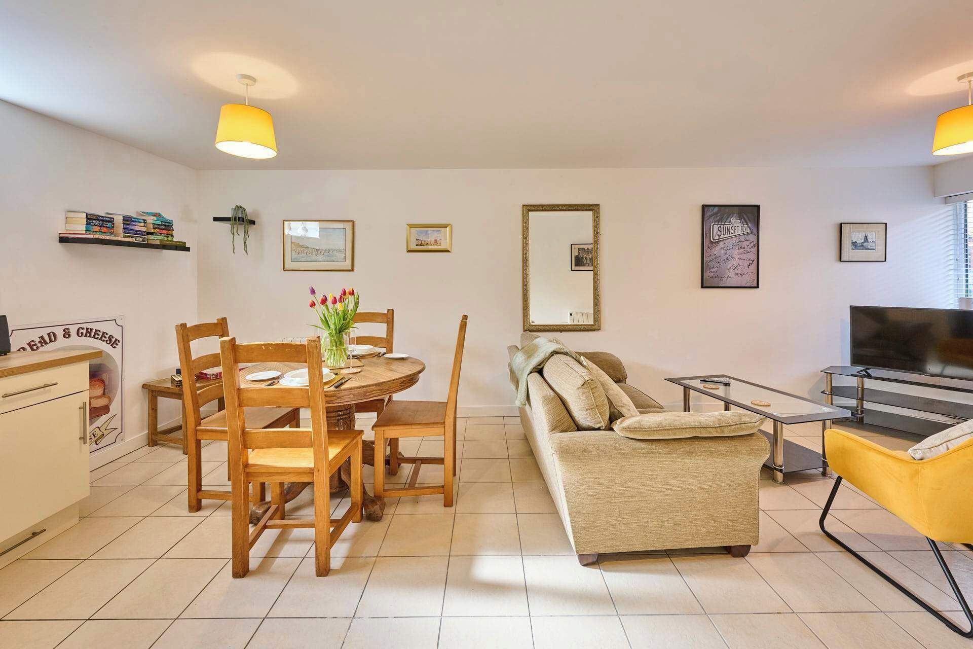 A living room with a round dining table, wooden chairs, a sofa, a TV, and a bookshelf with books.