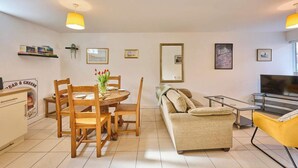 A living room with a round dining table, wooden chairs, a sofa, a TV, and a bookshelf with books. - Host & Stay | Nile Street Retreat (Norwich)