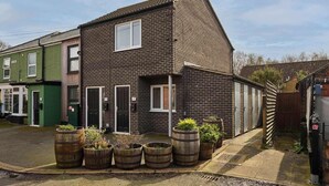 A two-story brick house with a pitched roof, numbered doors, and a small garden with barrel planters. - Host & Stay | Nile Street Retreat (Norwich)