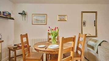 A dining area with a round wooden table, four wooden chairs, a vase of tulips, and two framed pictures on the wall.