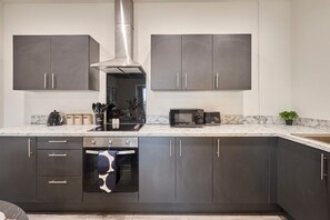 A modern kitchen with dark cabinets, a stainless steel range hood, a microwave, and a built-in oven. - Host & Stay | 18 Queens Court (Merseyside)