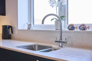 A kitchen with a stainless steel sink, a coffee maker, and decorative fish on the windowsill. - Host & Stay | Abbey View House (Whitby)