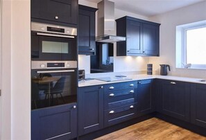 A modern kitchen with dark cabinetry, stainless steel appliances, and a window providing natural light. - Host & Stay | Abbey View House (Whitby)
