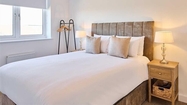 Een slaapkamer met een groot bed, nachtlampjes, een raam en een radiator.