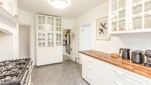 Una cocina con alacenas blancas, estufa a gas, encimera de madera y cafetera.