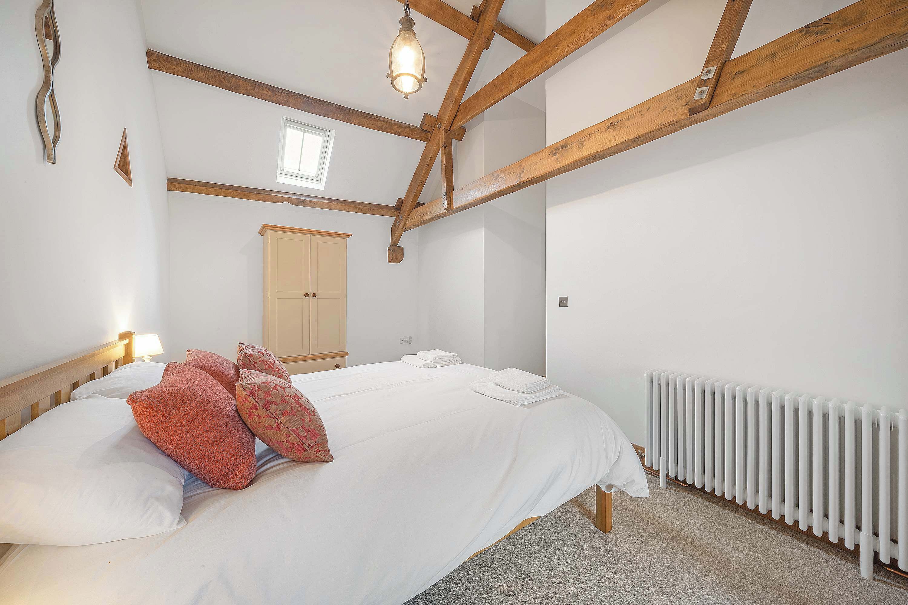 A bedroom with a bed, wooden beams, a radiator, and a window.