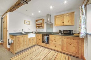 A kitchen with wooden cabinets, a built-in oven, a microwave, and a sink. - Host & Stay | The Cart House (Cwmdu)