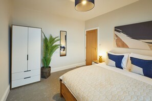 A bedroom with a bed, a wardrobe, a potted plant, a mirror, and a door. - Host & Stay | Flat 2 @ Temperance House (Saltburn-By-The-Sea)