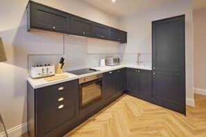 A modern kitchen with dark cabinetry, a microwave, a toaster, and a wooden cutting board. - Host & Stay | Flat 2 @ Temperance House (Saltburn-By-The-Sea)
