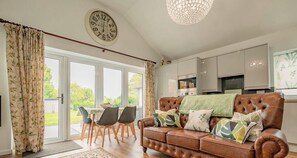 A spacious living area with a leather sofa, dining table, chairs, and a large window. - Host & Stay | Little Highlands (Tenbury Wells)