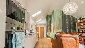 Una cocina moderna con electrodomésticos integrados, un comedor con sillas de cuero y un ventanal con vistas a un bosque.