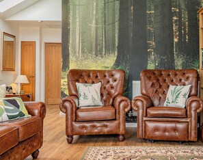 A room with two brown leather armchairs, a wooden floor, a patterned rug, and a forest-themed wall mural. - Host & Stay | Little Highlands (Tenbury Wells)