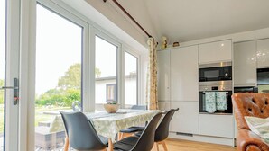 Una cocina moderna con electrodomésticos integrados, un comedor con mesa y sillas, y grandes ventanales que ofrecen vistas al exterior.