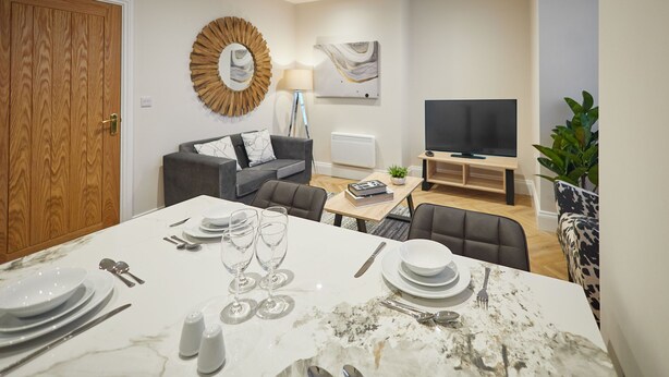 Una sala de estar moderna con comedor, televisor y un espejo grande.