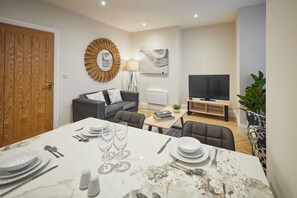 En moderne stue med spiseplads, fjernsyn og et stort spejl.