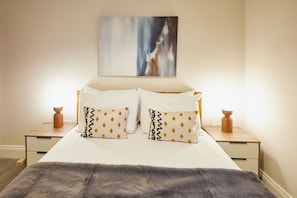 A bed with white linens and patterned pillows, a gray throw blanket, and a painting above. - Host & Stay | Flat 1 @ Temperance House (Saltburn-By-The-Sea)