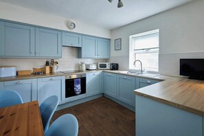 Een moderne keuken met lichtblauwe kastjes, een houten aanrecht, een ingebouwde oven, een magnetron, een koffiezetapparaat en een groot raam.