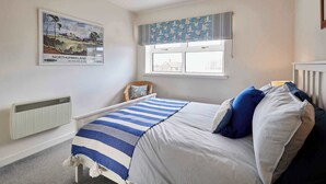 Een slaapkamer met een bed, een raam met gordijnen, een radiator en een poster aan de muur.