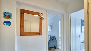 Een gang met een spiegel met houten lijst, een welkomstbord en een deur die leidt naar een slaapkamer met een bed en een blauwe bank.
