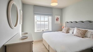 Ein Schlafzimmer mit Bett, Nachttisch, Spiegel, Fenster und Kunstwerk.