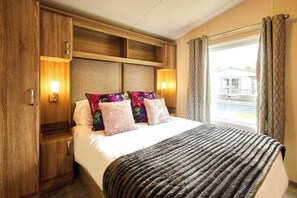 Une chambre d’hôtel avec un lit, une tête de lit en bois, deux lampes fixées au mur, une fenêtre avec des rideaux et une vue sur un bâtiment à l’extérieur.