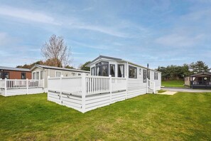 Une maison mobile dotée d’une terrasse clôturée, d’un porche abrité et d’une cour gazonnée.