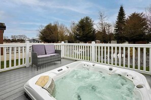 Un bain à remous sur une terrasse dotée d’une balustrade blanche, un canapé en osier et des arbres en arrière-plan.