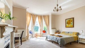 Ein Schlafzimmer mit einem Bett, einem Schreibtisch, einem Sessel, einem Kamin und einem Fenster mit Vorhängen.
