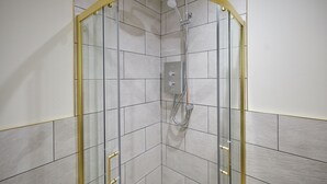 Eine Duschkabine mit gebogener Glasduschtür, einer Handbrause und einer fest installierten Bedienpanel an der Wand.