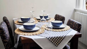 Ein Esstisch ist gedeckt mit blauen Schalen und Weingläsern, umgeben von stuhligen Sitzgelegenheiten mit Muster.
