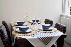Ein Esstisch ist gedeckt mit blauen Schalen und Weingläsern, umgeben von stuhligen Sitzgelegenheiten mit Muster.