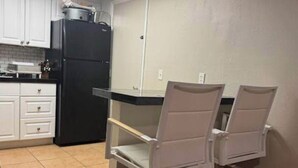 A kitchen with white cabinets, a black refrigerator, and two white chairs. - 2 BR 2 BA Condo  (Cape Canaveral)