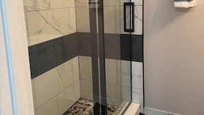 A modern bathroom with a glass shower enclosure, a tiled floor, and a towel hanging on the wall. - 2 BR 2 BA Condo  (Cape Canaveral)