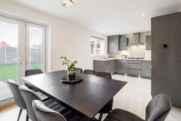 A modern dining area with a dark wooden table, grey upholstered chairs, and a potted plant.
