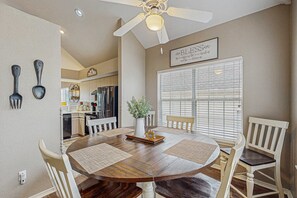 A dining area with a round table, white chairs, a ceiling fan, and a kitchen in the background. - GOLF VIEWS - Spacious 3BR Condo with Loft & Pool (Branson)