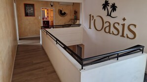 Una escalera con barandilla que lleva a una plataforma, una pared con la palabra 'Oasis' y adornos de palmeras, y un cuadro enmarcado en la pared.