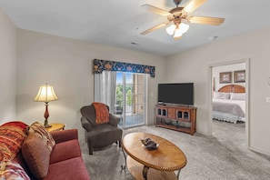 A living room with a sofa, armchair, coffee table, TV stand, and a ceiling fan. - Spacious 2BR Condo - GOLF VIEWS - Pool & Dogs ok (Branson)