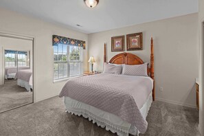 A bedroom with a large bed, a window with blinds, a mirror, and two framed pictures on the wall. - Spacious 2BR Condo - GOLF VIEWS - Pool & Dogs ok (Branson)