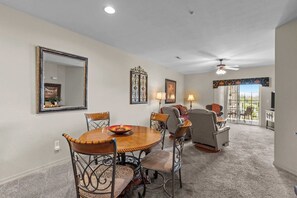 A dining area with a round table and chairs, a large mirror, and a ceiling fan. - Spacious 2BR Condo - GOLF VIEWS - Pool & Dogs ok (Branson)