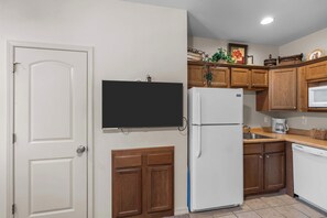 A compact kitchen with wooden cabinets, a built-in refrigerator, a microwave, and a wall-mounted television. - Spacious 2BR Condo - GOLF VIEWS - Pool & Dogs ok (Branson)