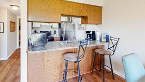 A modern kitchen with wooden cabinets, stainless steel appliances, a granite countertop, and two bar stools. - Pointe Royale - 1BR/1B - pools and fitness center (Branson)