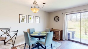 A dining area with a round table, chairs, a chandelier, artwork on the wall, and a view through a large window. - Pointe Royale - 1BR/1B - pools and fitness center (Branson)