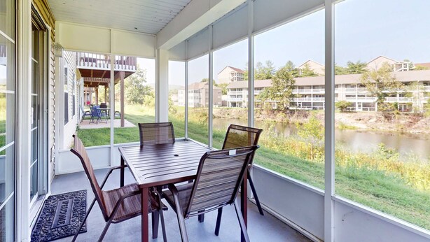 Une terrasse couverte avec une table et des chaises, de grandes fenêtres et une vue sur un plan d’eau et des bâtiments.
