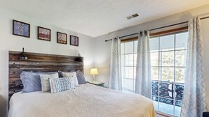 Une chambre à coucher avec une tête de lit en bois, un lit recouvert d’une couverture à motifs, une table de chevet avec une lampe et une fenêtre avec des rideaux.