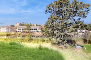 A building with multiple floors, a pond, and a large tree in the foreground. - POND VIEW - Pet-Friendly 2BR Condo in Branson (Branson)