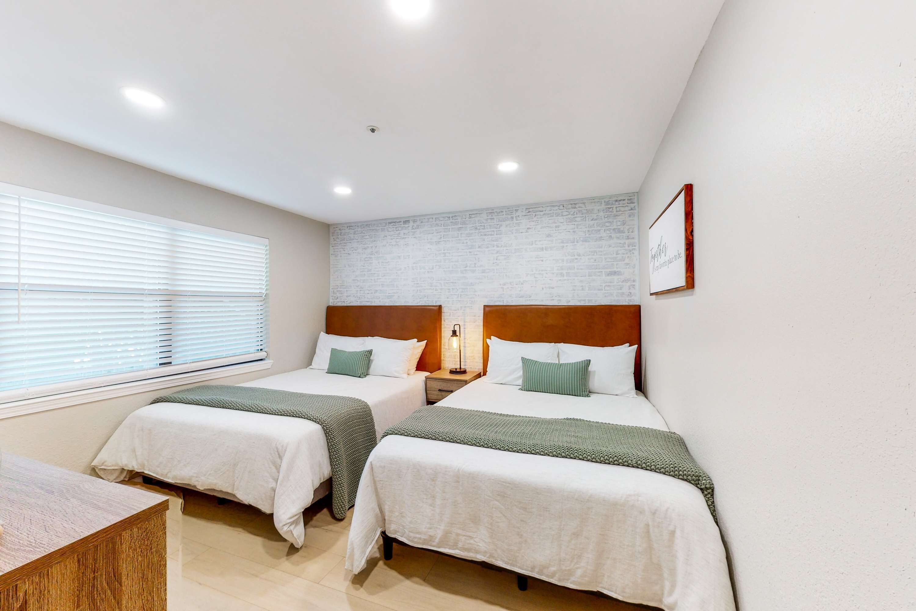 Une chambre d’hôtel avec deux lits, une petite table, une table de chevet avec une lampe et un mur décoré d’un motif en briques.
