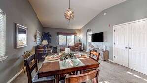 A dining area with a wooden table, chairs, a hanging light fixture, and a television mounted on the wall. - Inviting 2BR Condo - HOT TUB - Family Pool (Branson)